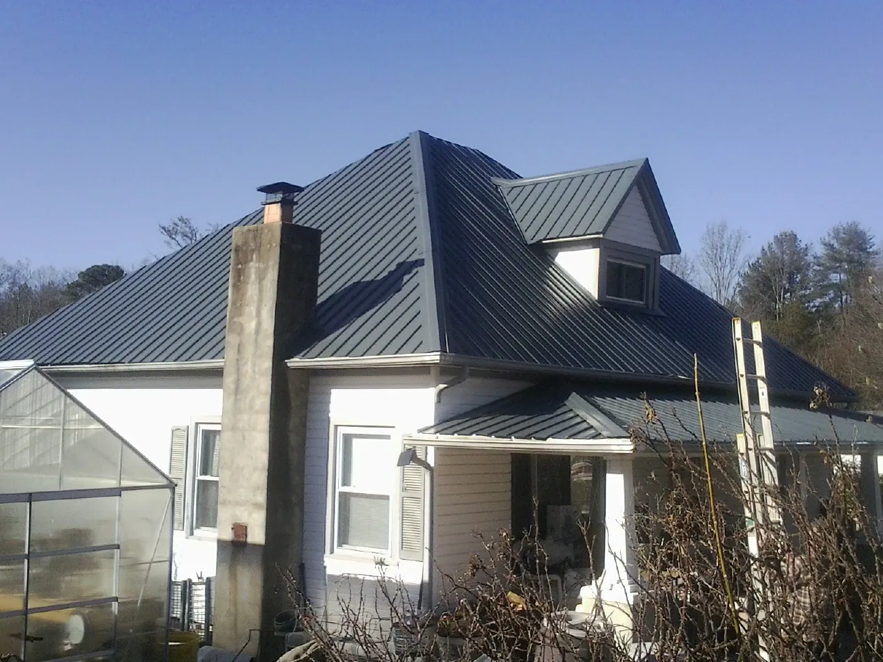 Dark blue standing seam metal roof on a white farmhouse with dormer — Slate & Tile Roof Repair by Roofing Brothers in Blue River