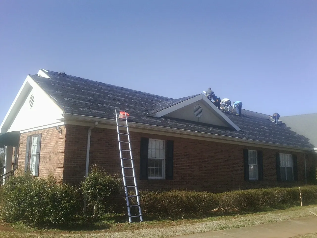 Crew tearing shingles off a brick ranch roof with a ladder set — Metal Roof Repair work by our crew in Blue River