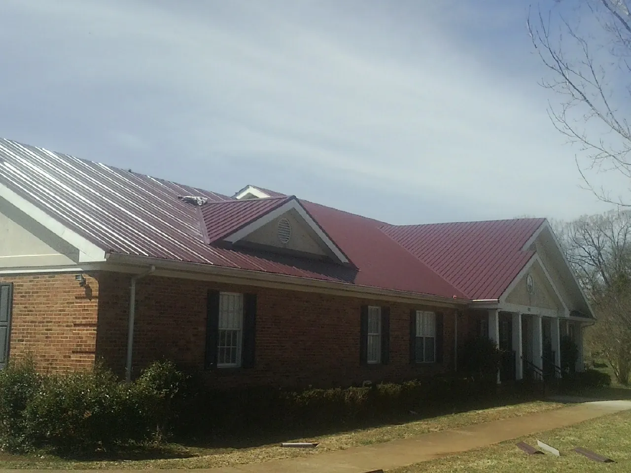 Red metal roof with gabled entries on a long brick building, from a Hail Damage Roof Repair job in Blue River