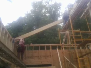 Carpenter raising a rafter beam on a new second story frame in Blue River