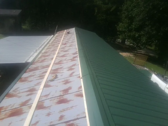 Old rusted panels beside newly installed green metal roofing — Wind Damage Roof Repair by Roofing Brothers in Blue River
