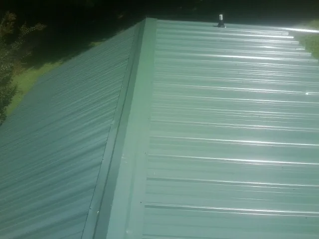 New green metal panels meeting at the ridge of a roof — Flat Roof Repair work by our crew in Blue River