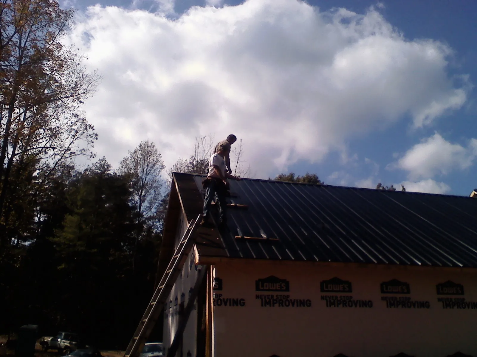 Roofer fastening dark metal panels high against a cloudy sky, from a Roof Inspection job in Blue River