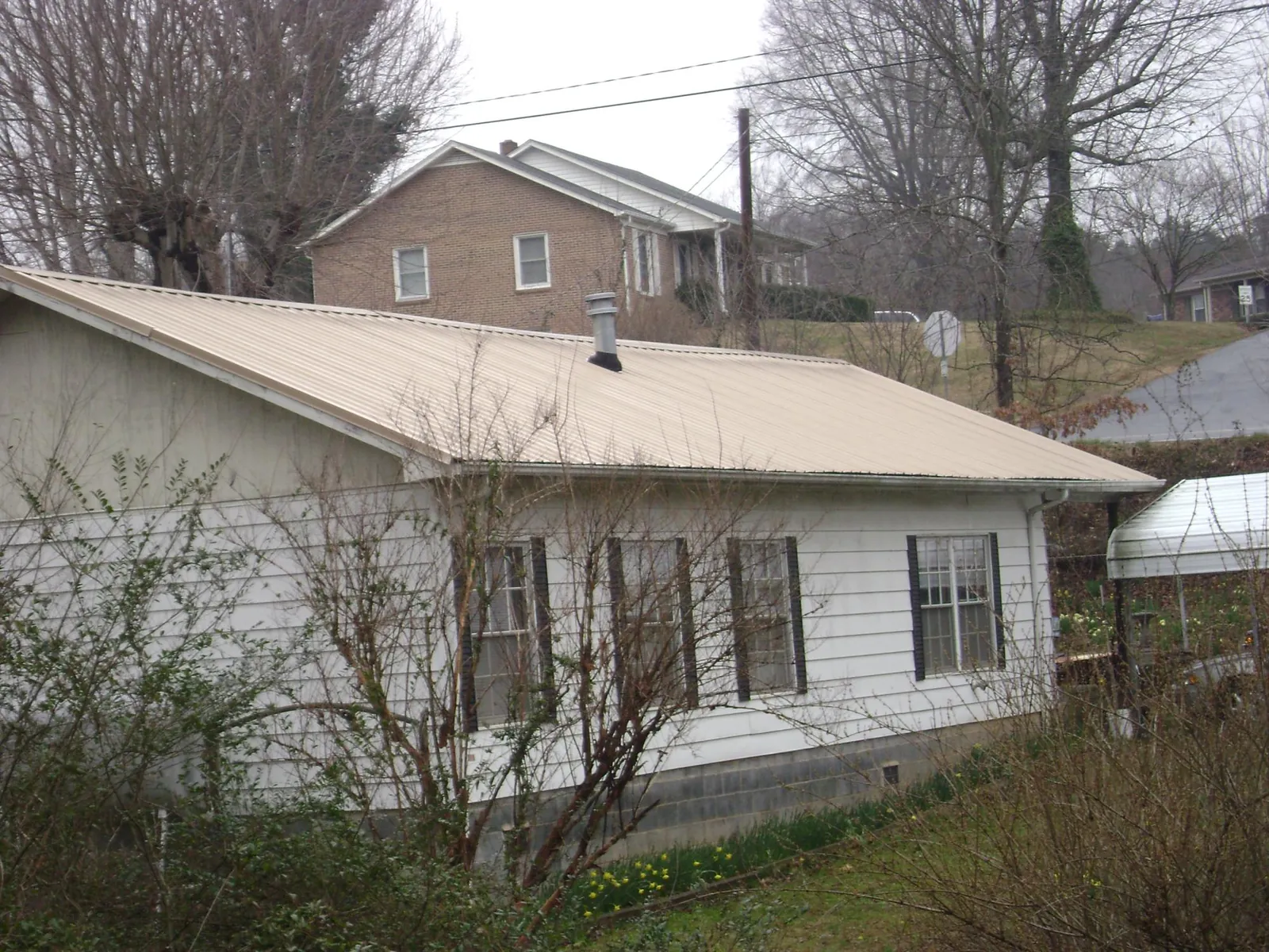 Tan metal roof on a white sided house set into a hillside — Commercial Roofing by Roofing Brothers in Blue River