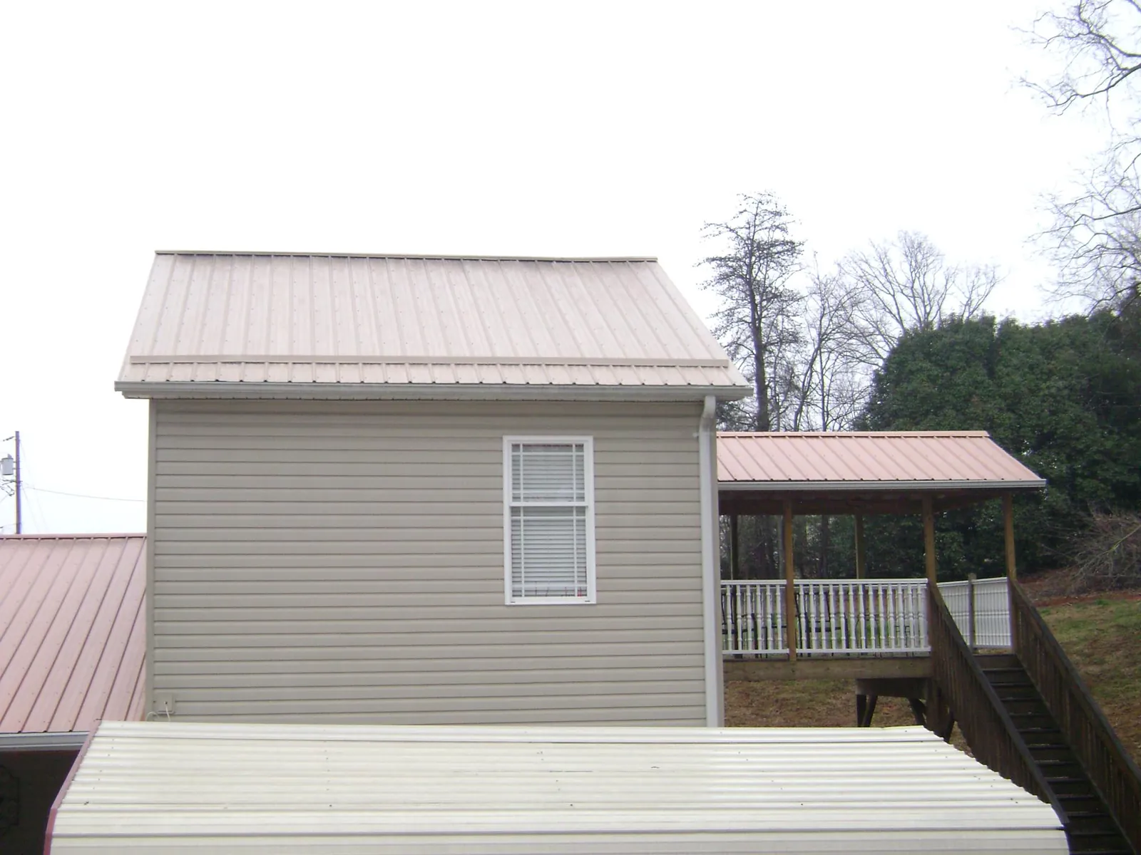 Tan metal roofs on a two story addition and attached porch, from a Roof Replacement job in Blue River